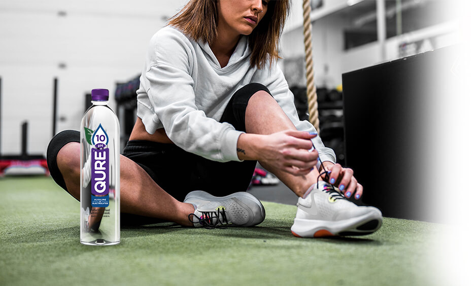 A woman with QURE 10pH Alkaline Water shoe lacing her shoes while preparing for a workout